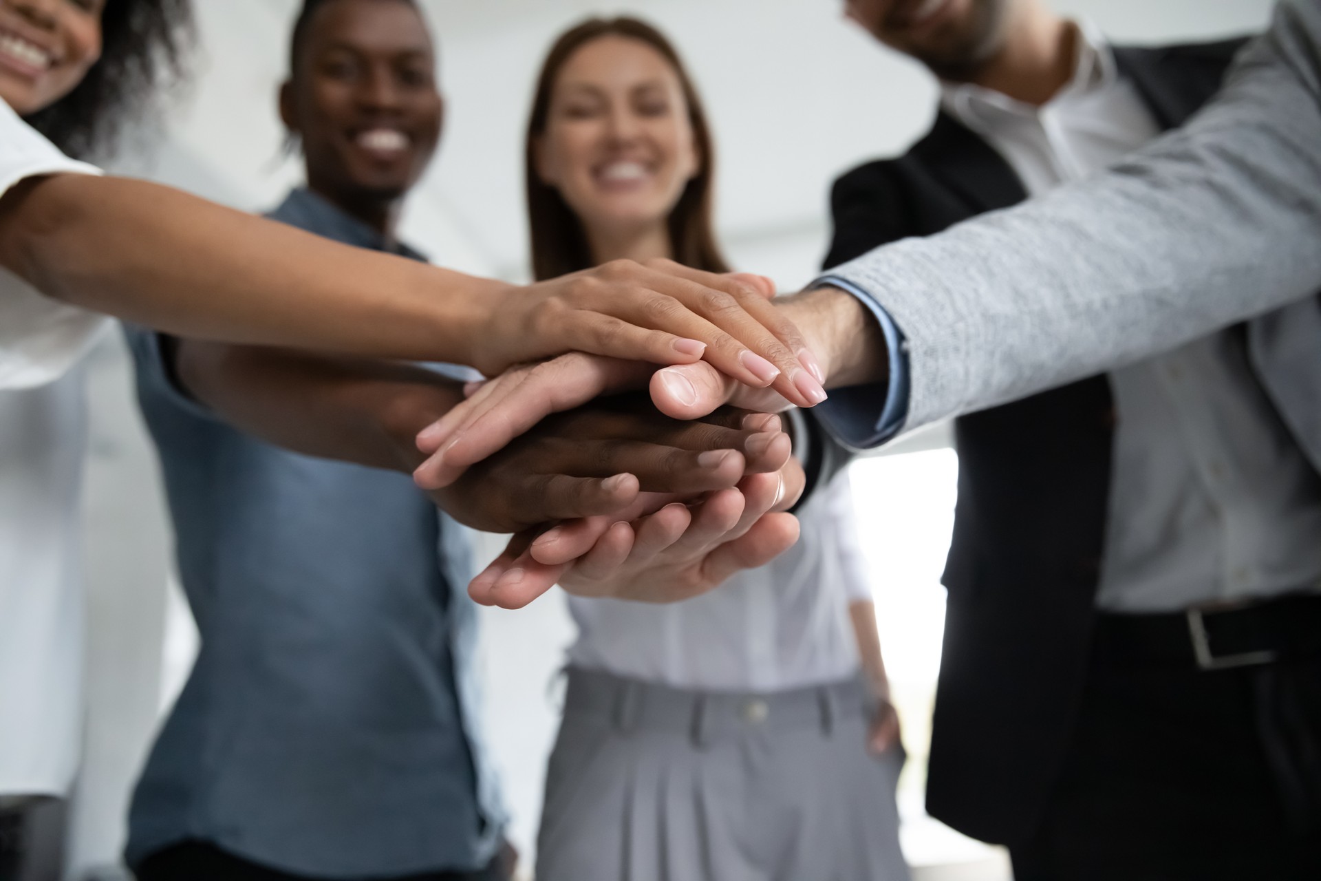 Close up happy diverse business people putting hands together.